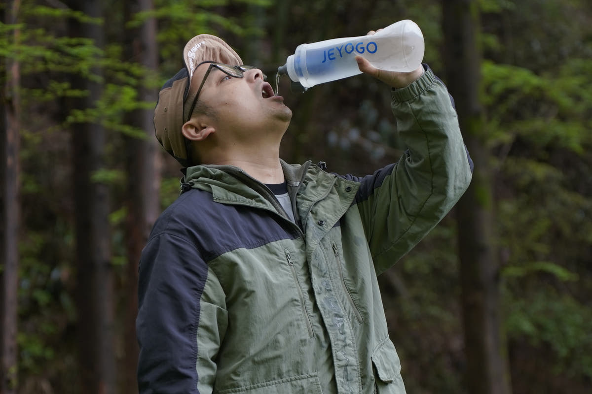 Drinking from the JEYOGO water filter bottle in a forest