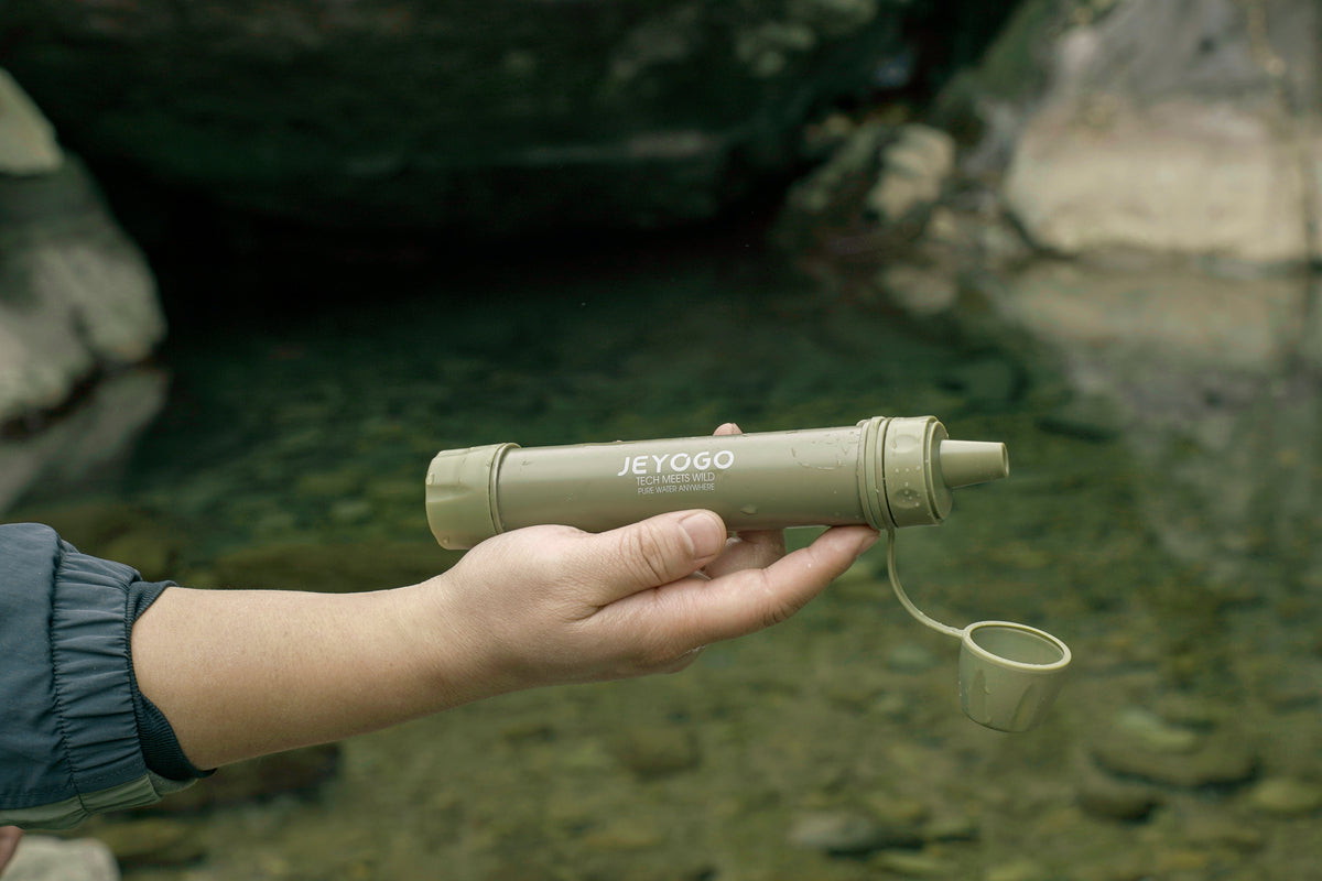 JEYOGO portable filter straw held beside an outdoor freshwater stream
