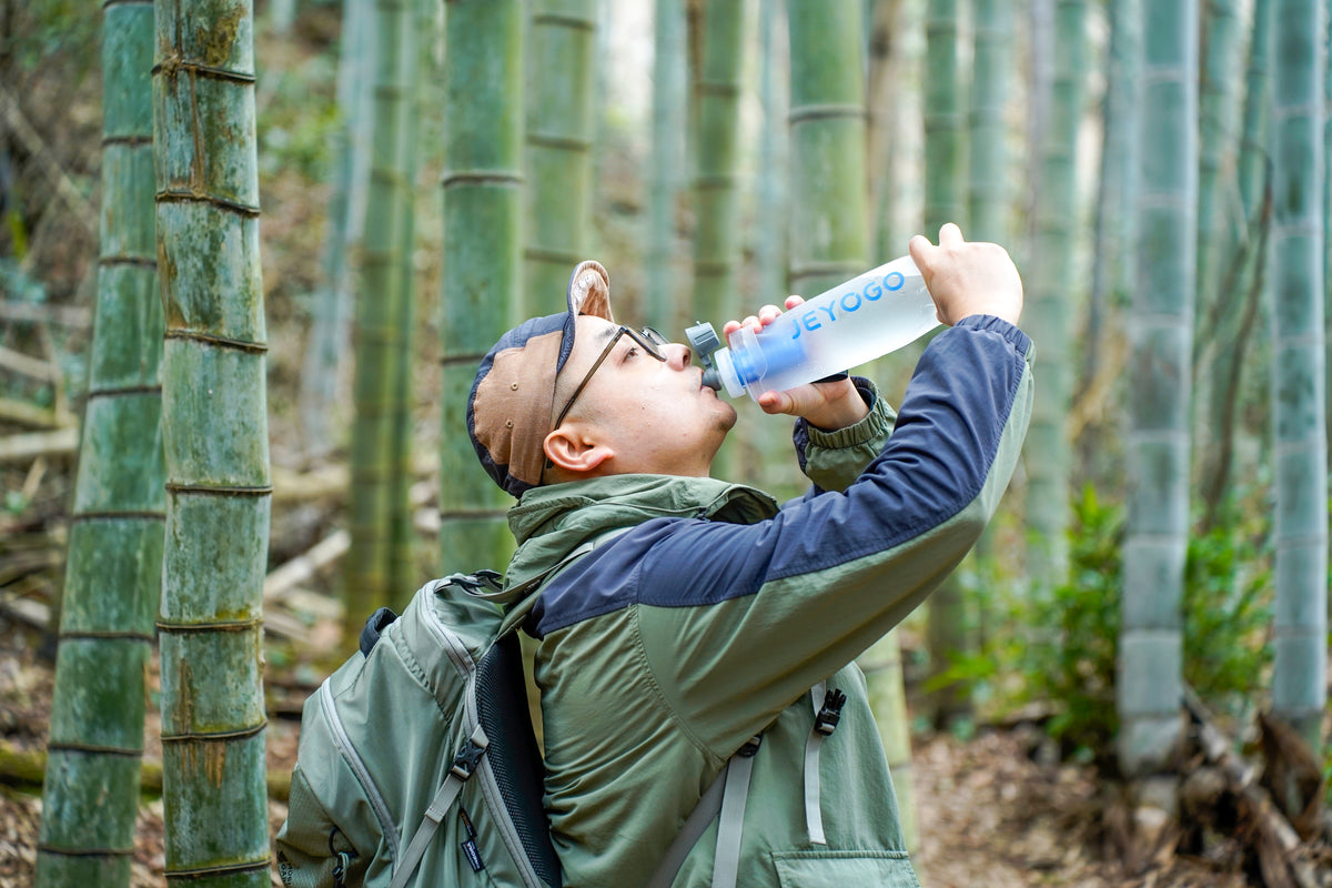 Hiker drinking from a JEYOGO collapsible water filter bottle in a bamboo forest